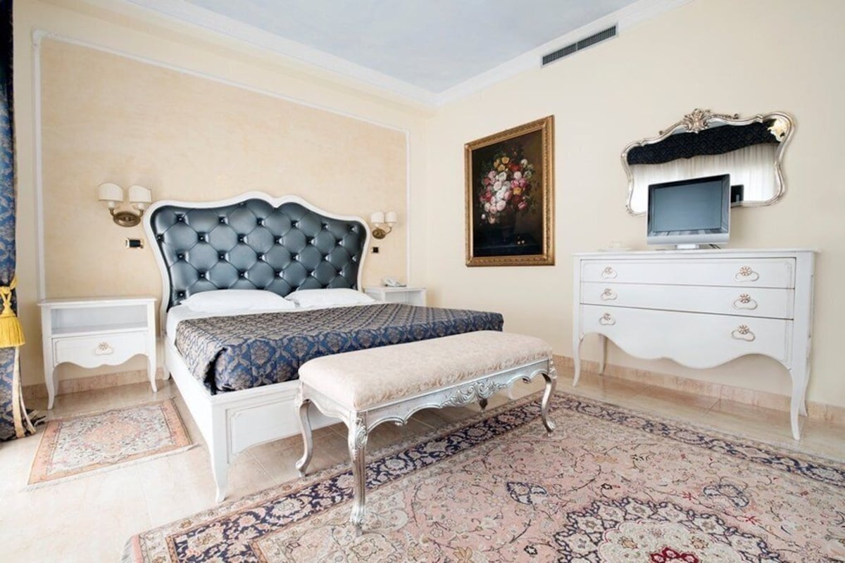 Een slaapkamer met een bed, nachtkastjes, een televisie, een dressoir en een kamerbreed tapijt met een patroon.
