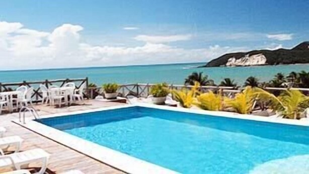 A swimming pool with lounge chairs and a view of the ocean. - Maritima Flat (Natal)