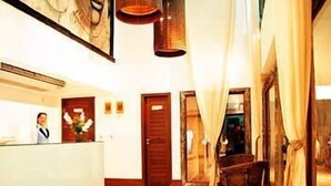 A hotel reception area with a receptionist, a reception desk, a wooden door, and a wicker chair. - Maritima Flat (Natal)