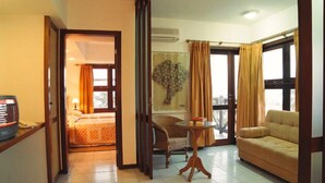 A hotel room with a bed, a sofa, a small table, a chair, and a view of the outdoors through a large window. - Maritima Flat (Natal)