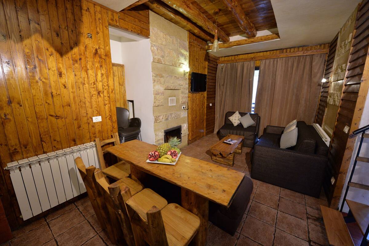 Ein Holzinnenraum mit Esstisch, Stühlen, einer Couch und einem Kamin.