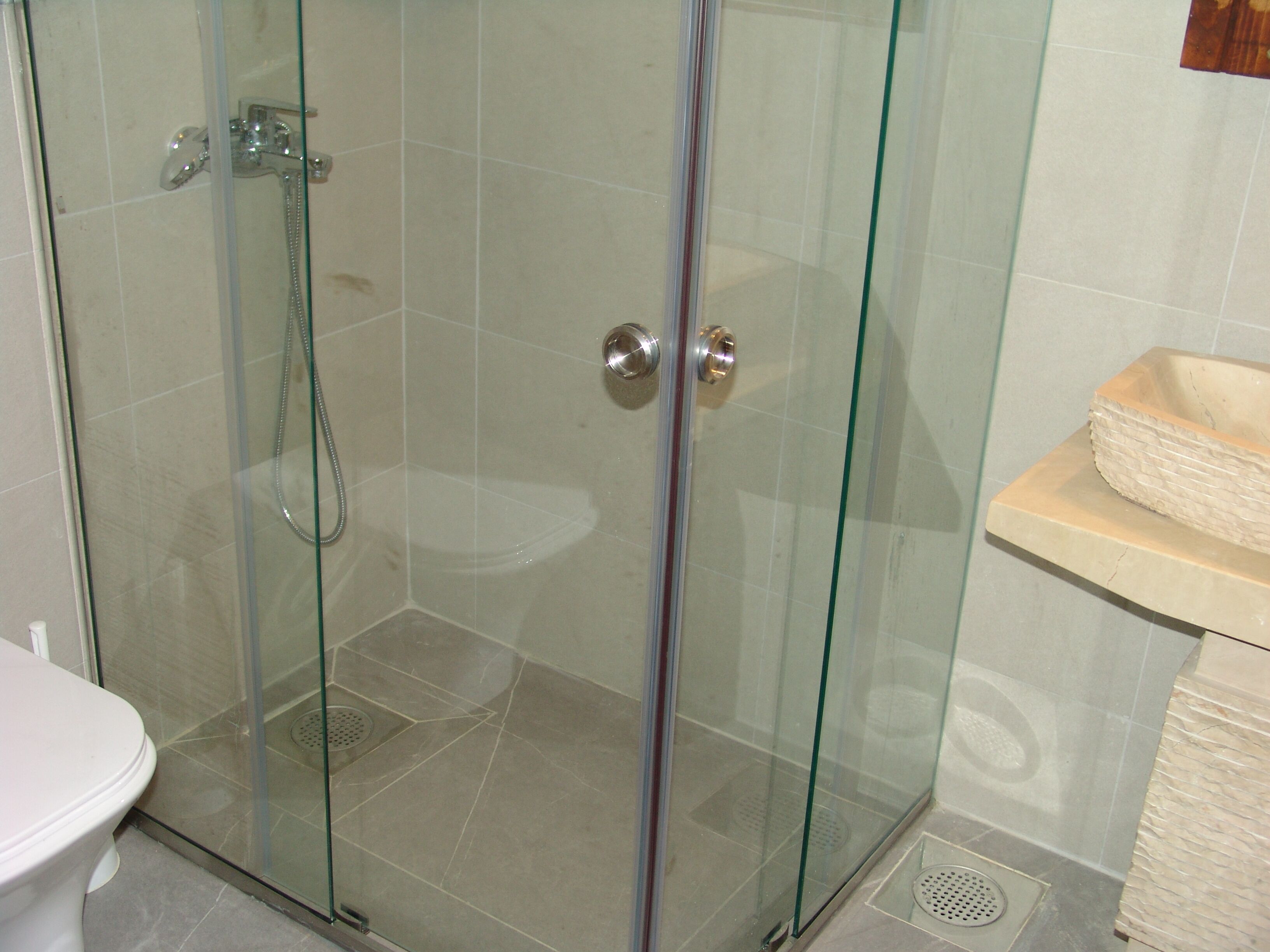 Ducha con cerramiento de vidrio, cabezal de ducha manual y grifo empotrado.