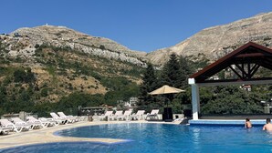 A swimming pool with lounge chairs and a pavilion, surrounded by mountains. - Faraya Village Club (Faraya)