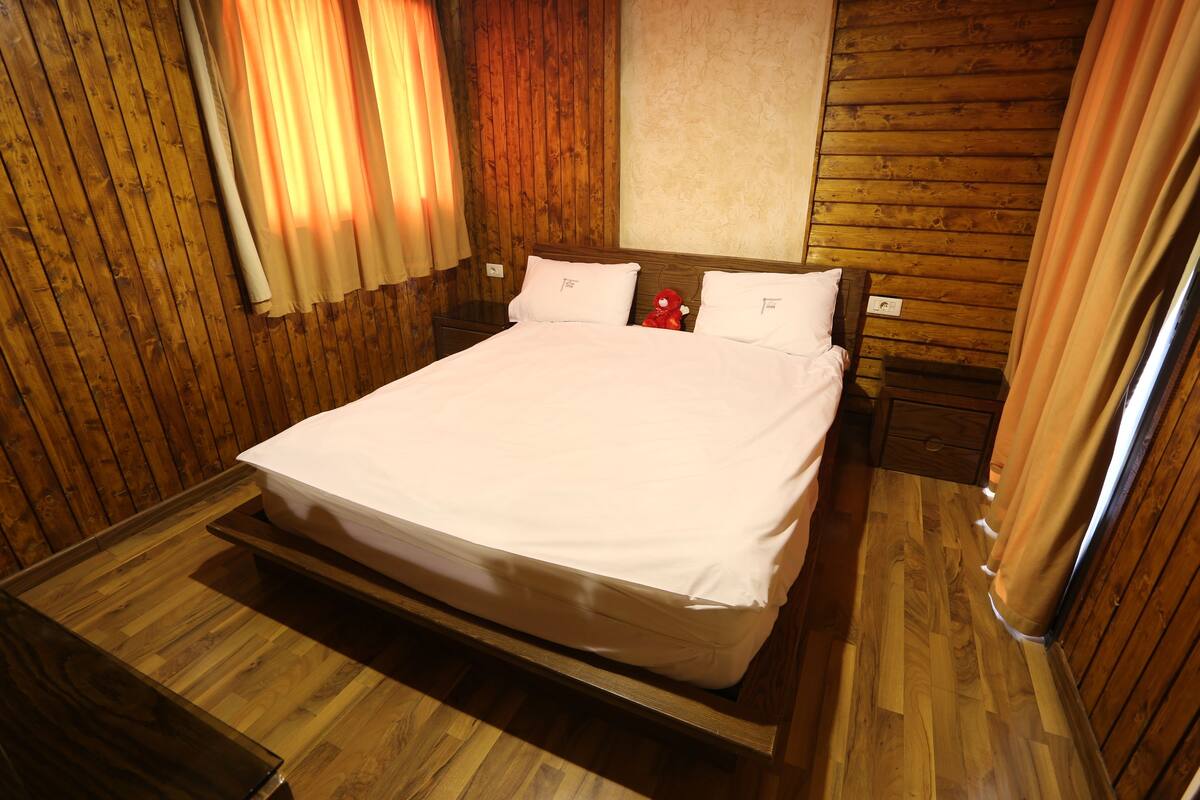 Ein Zimmer mit Holzwänden, einem Bett, Holzboden und Vorhängen.