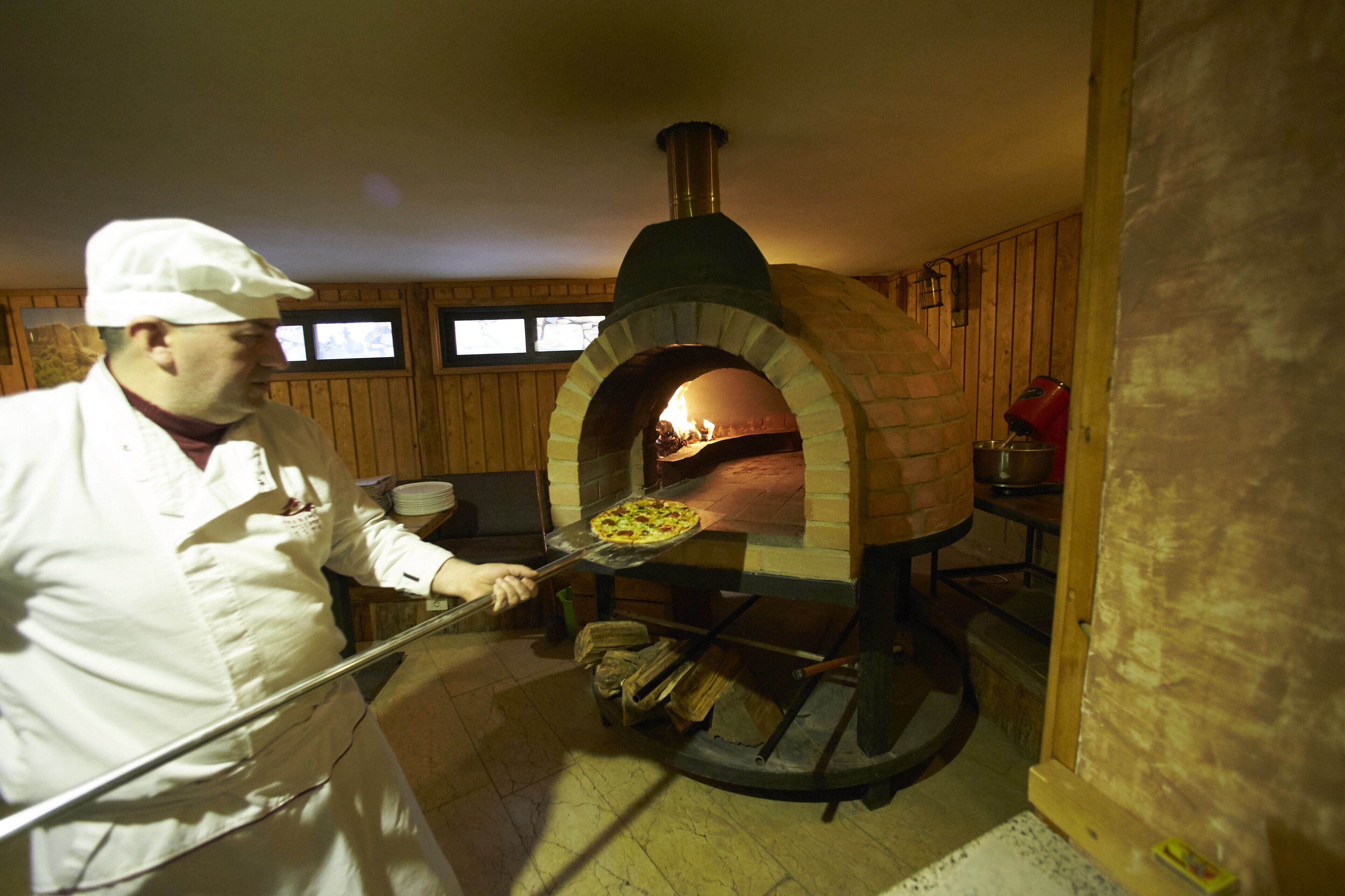 Une personne vêtue d'un uniforme de chef blanc, qui utilise un four à pizza en briques.