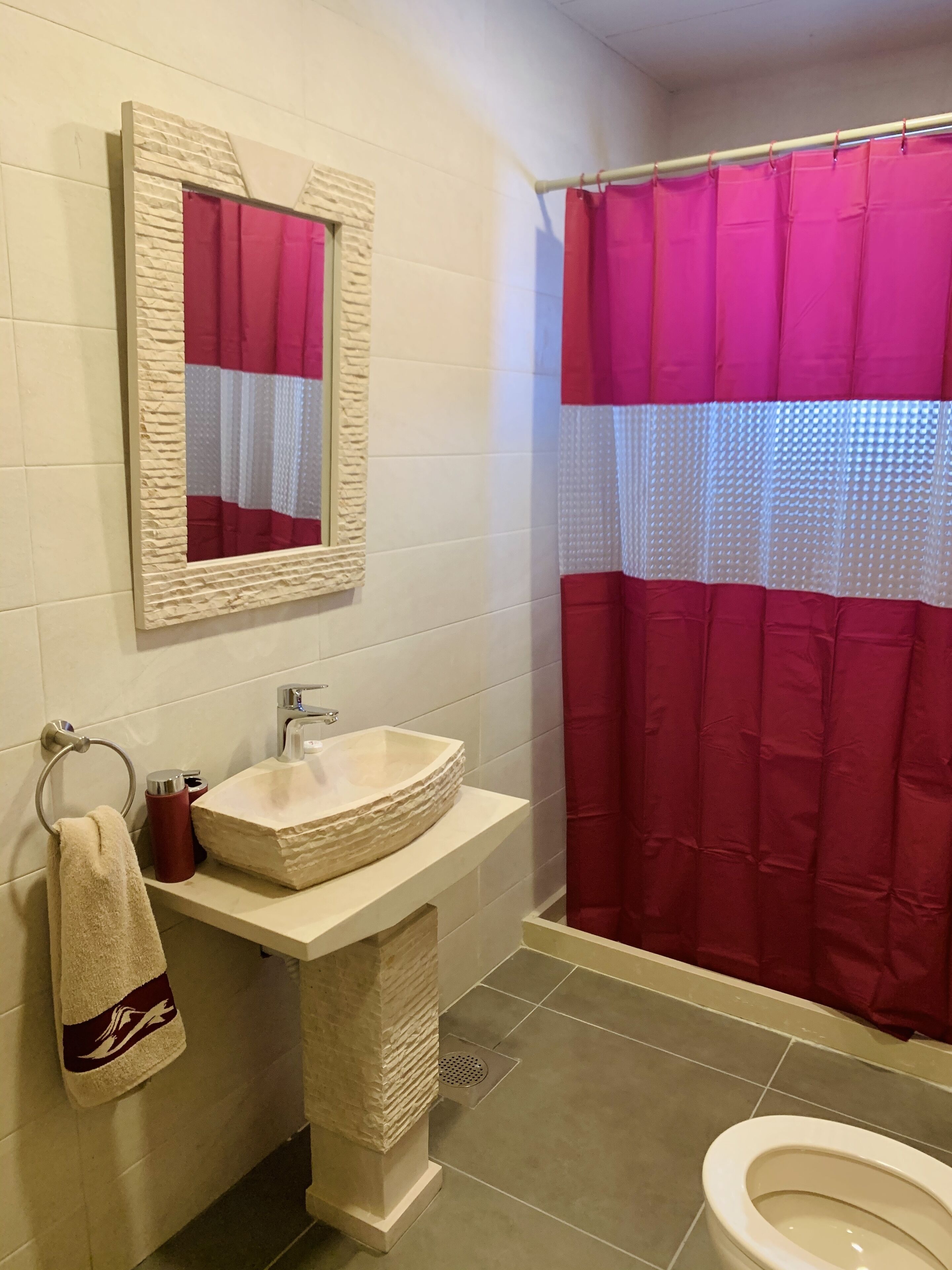 Un baño con lavamanos de piedra, un espejo, una toalla y cortina de ducha roja.