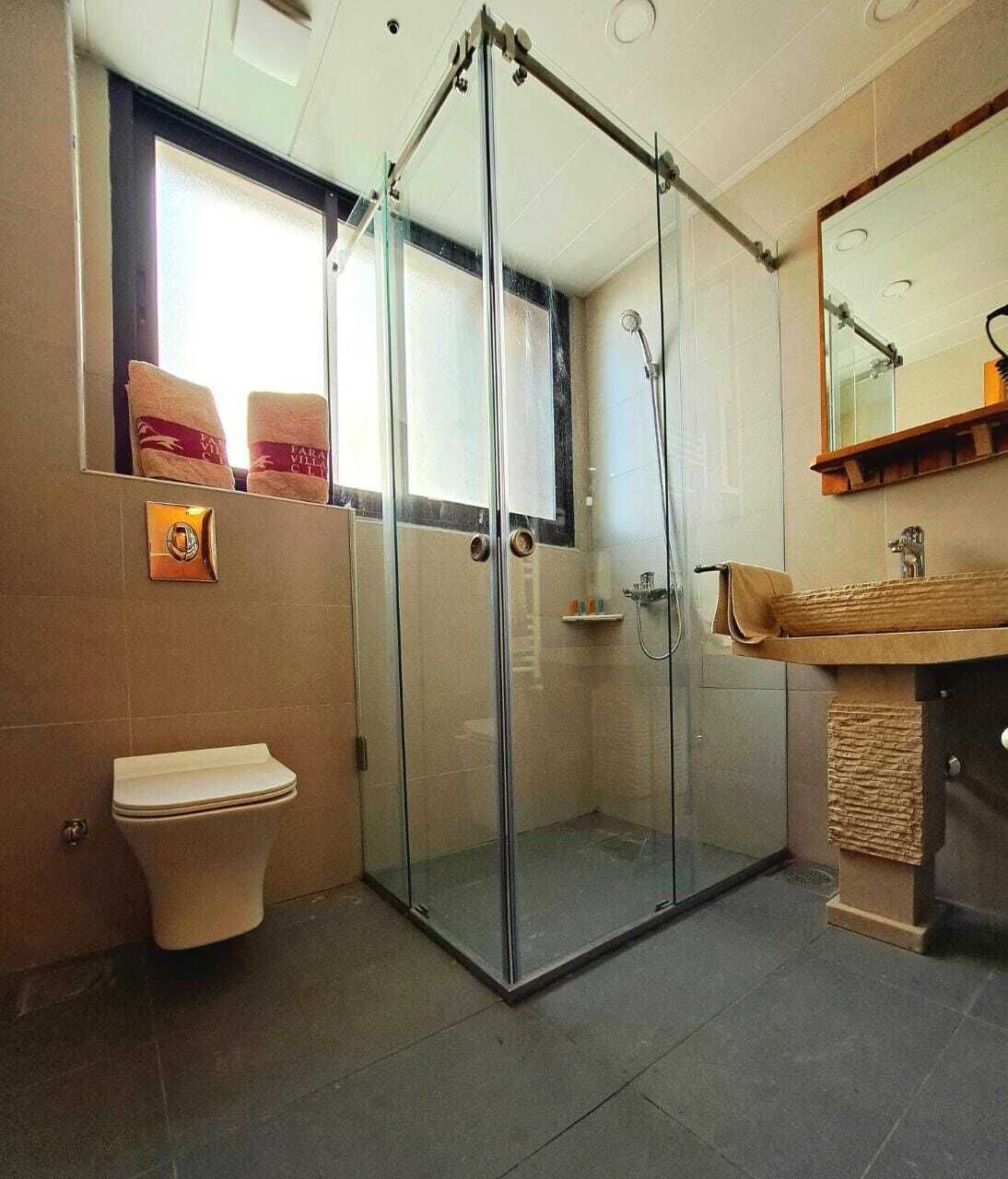 A bathroom with a glass-enclosed shower, a toilet, and a sink with a towel rack.