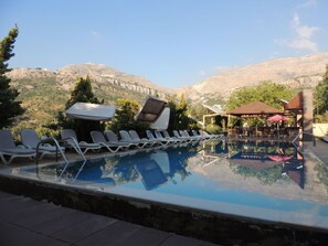 Una piscina infinita con sillones de descanso y sombrillas, con vistas a un paisaje montañoso.