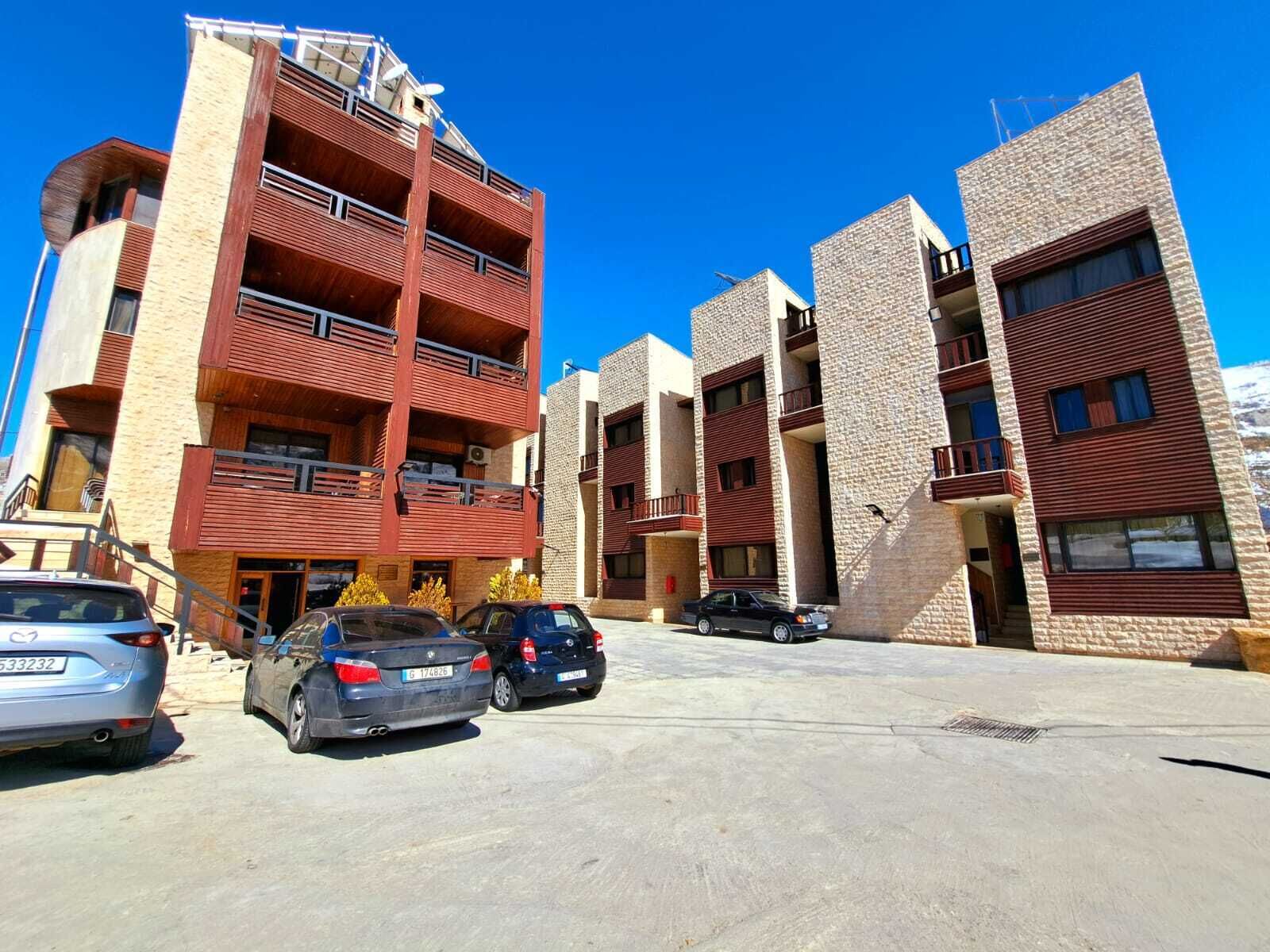 A multi-story residential building with balconies and a parking area.