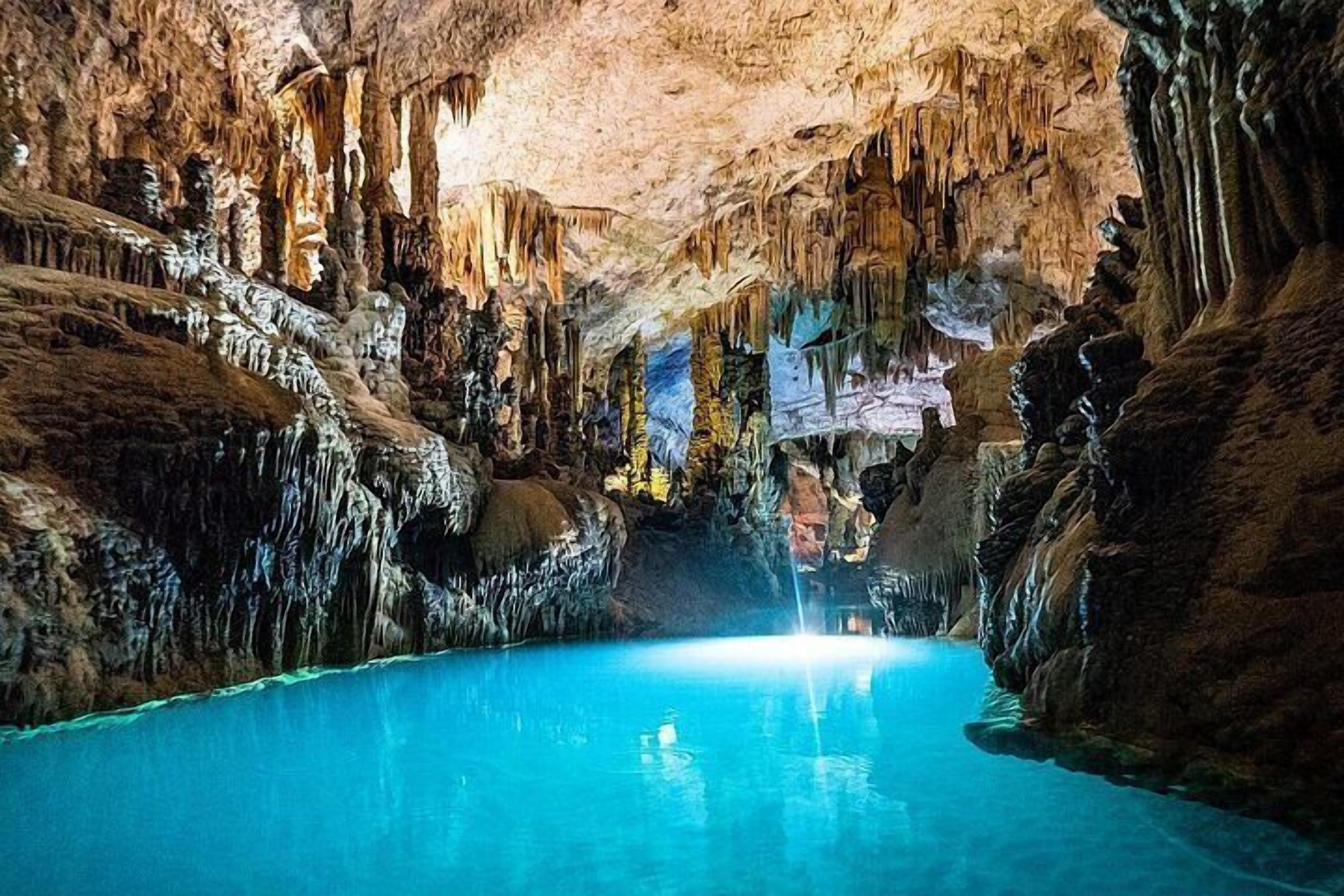 Eine Höhle mit Stalaktiten und Stalagmiten, ein Wasserbecken und eine Person in der Mitte.