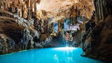 A cave with stalactites and stalagmites, a pool of water, and a person in the center.