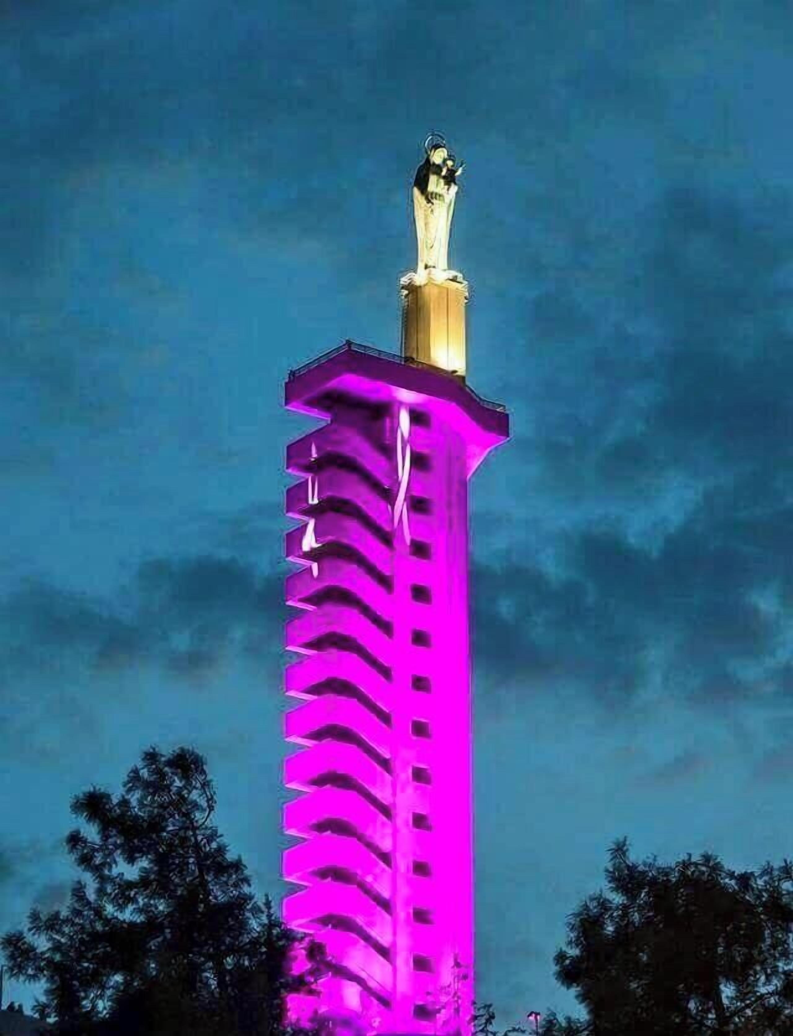 En høj bygning med en statue øverst, oplyst i lilla og guld.