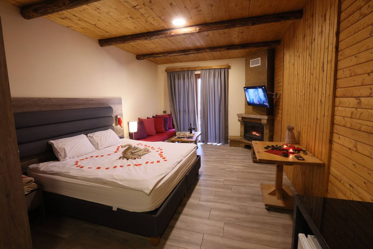 Ein gemütliches Zimmer mit einem Bett, einem kleinen Tisch mit Kerzen, einem Fernseher und einem Kamin.