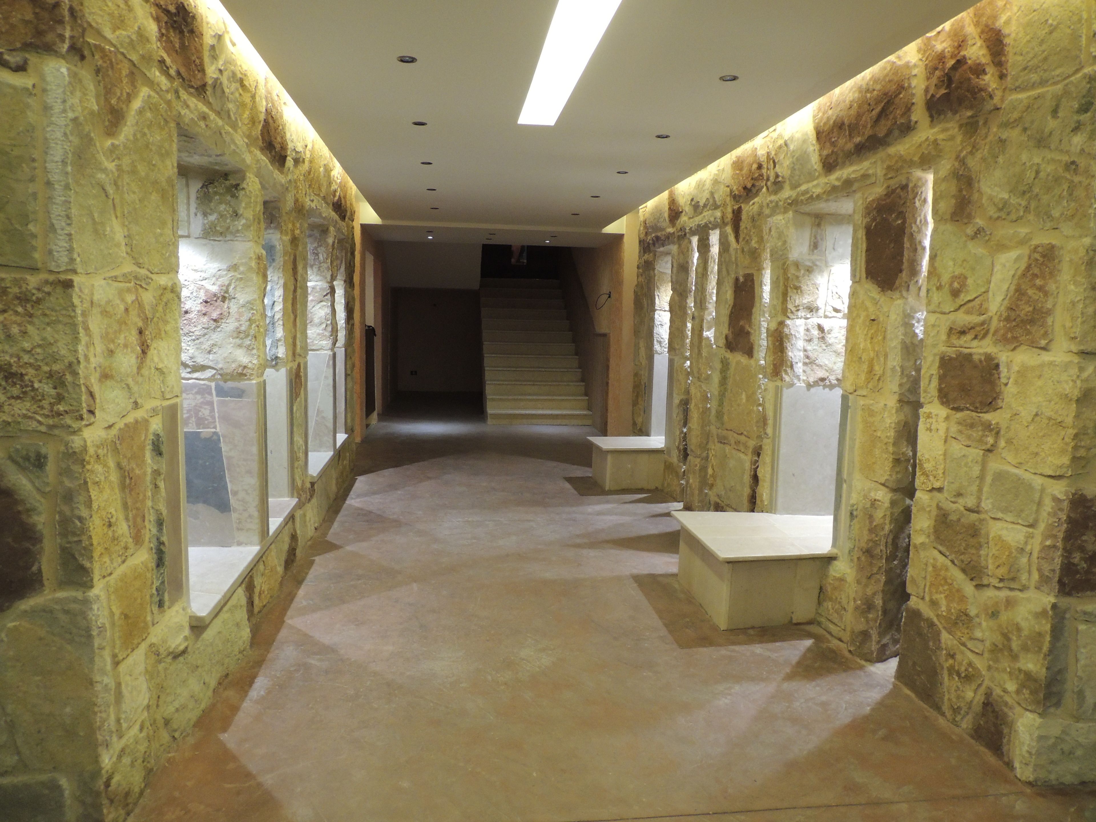 A hallway with stone walls and a tiled floor, leading to a staircase.