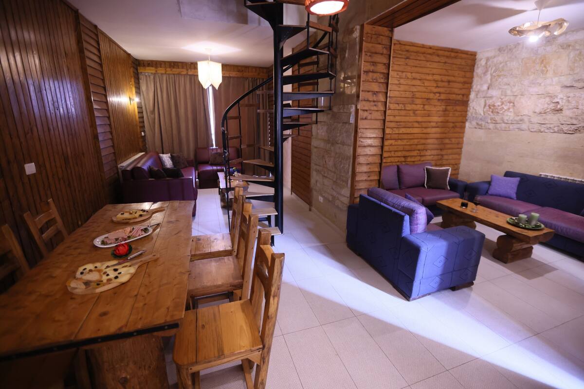 Ein Holzespeisesaal mit Stühlen, eine Sofagarnitur und eine Wendeltreppe.