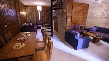 A wooden dining table with chairs, a sofa set, and a spiral staircase.