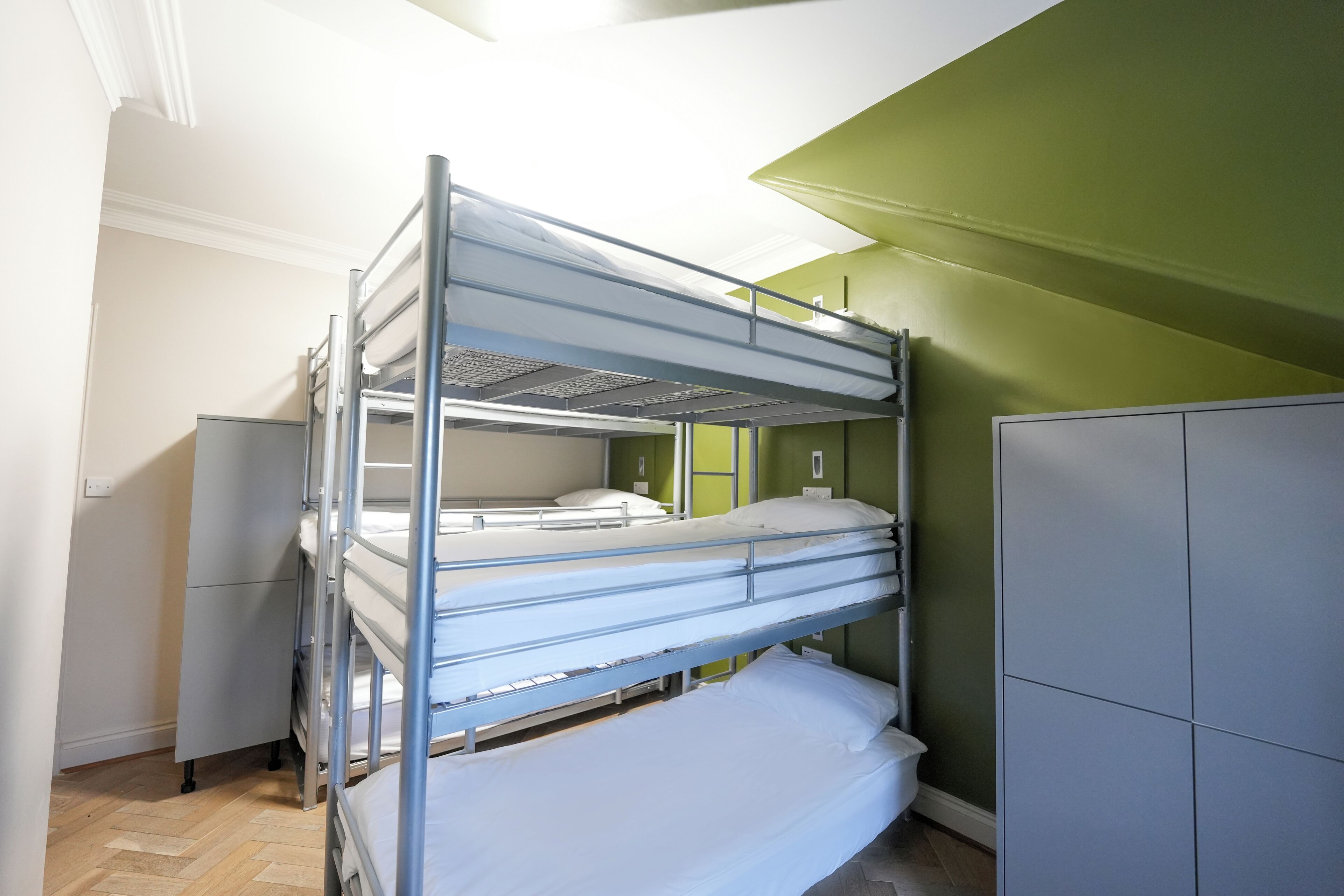 A bunk bed room with a green wall and a grey wardrobe.