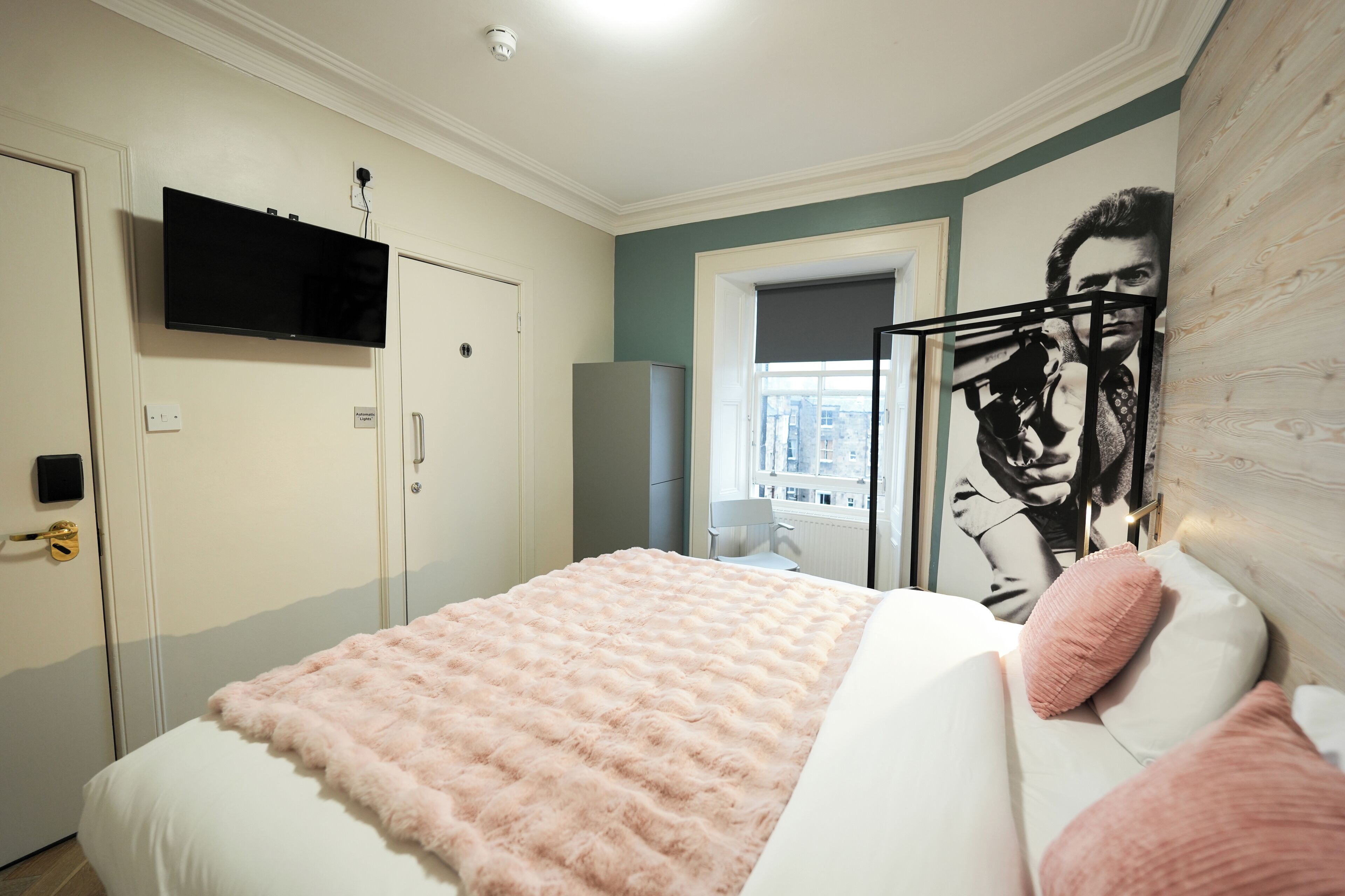 Une chambre à coucher avec un lit, un téléviseur fixé au mur, une fenêtre donnant sur un paysage agréable et une porte dotée d’une poignée.