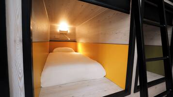 A compact room with a bed, a ladder, and a wall-mounted light fixture.