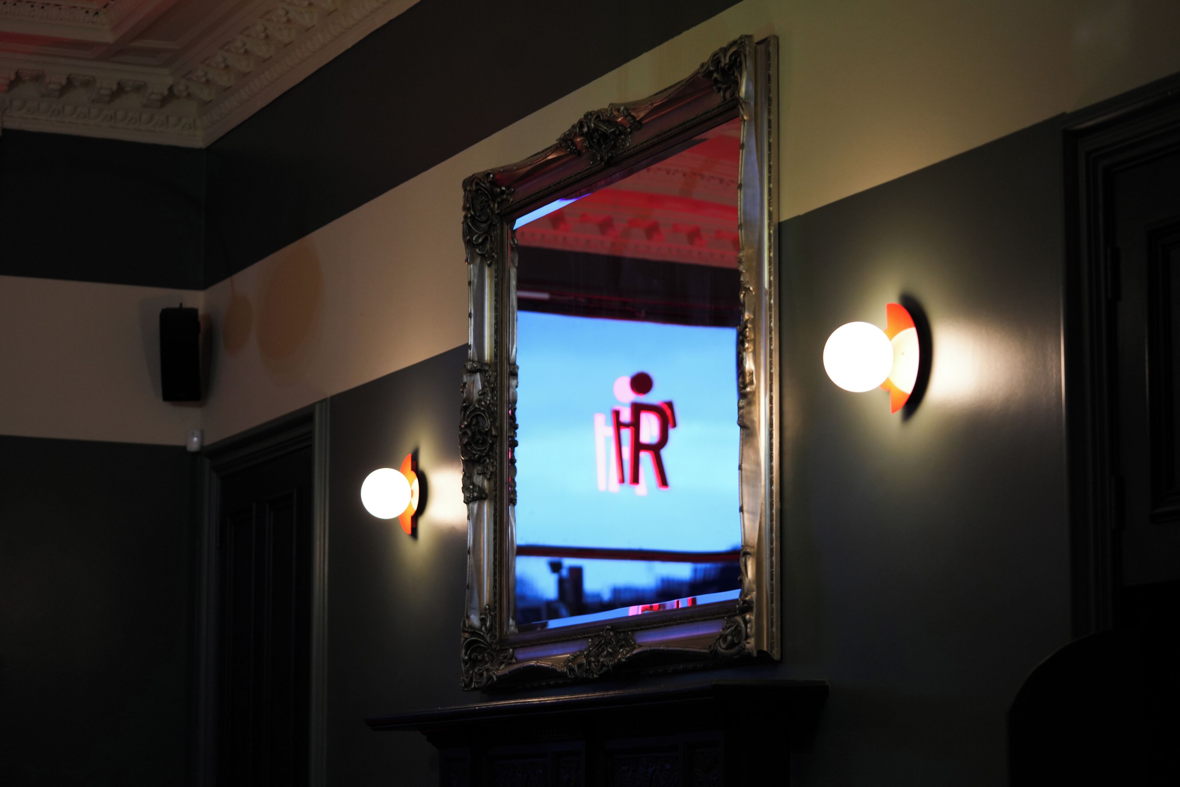 A mirror with a decorative frame reflecting a room with a red ceiling and wall sconces.