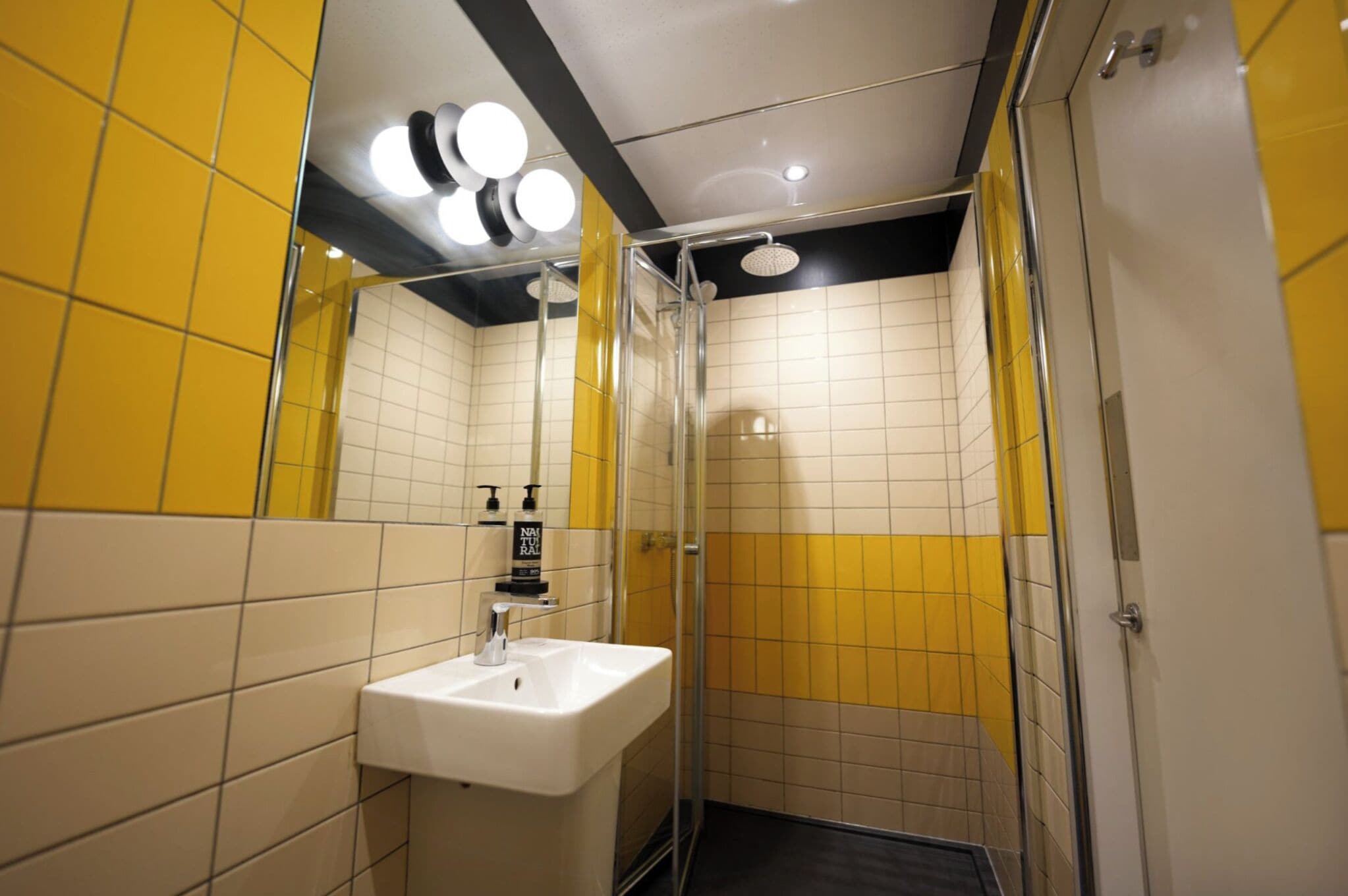 A bathroom with yellow and white tiles, a sink, and a glass-enclosed shower.