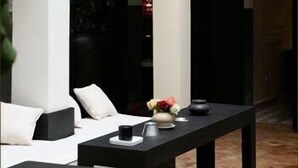 Quarto moderno e minimalista com uma mesa preta, almofadas brancas e um vaso com flores.