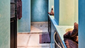 Um corredor estreito com chão de azulejos, uma porta escura e uma parede azul com um arco decorativo.