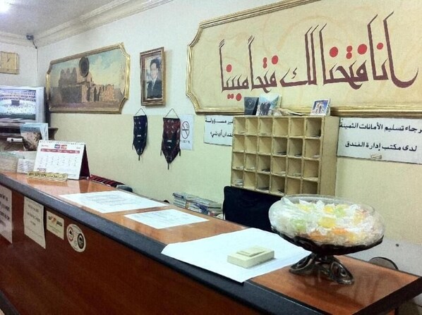 A reception desk with a calendar, a framed portrait, and a wall sign in Arabic.