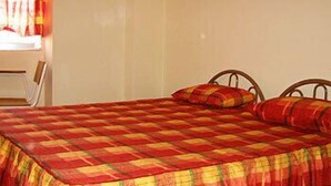 Una cama con una colcha a cuadros, un cabecero de madera y una ventana con cortinas.