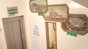 Un pasillo con un cartel del Farah Hotel, un letrero de salida y dos cuadros con imágenes de sitios históricos.