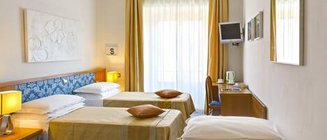 A hotel room with two beds, a desk, a television, and a large window with curtains.
