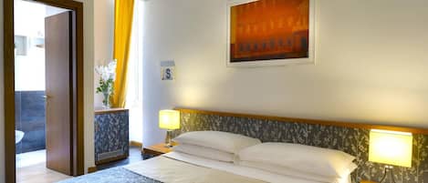 A hotel room with a bed, a nightstand, a lamp, a picture on the wall, and a window with curtains.
