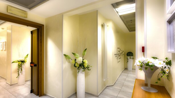Een hal met een houten deur, een witte vaas met bloemen en een houten receptiebalie.