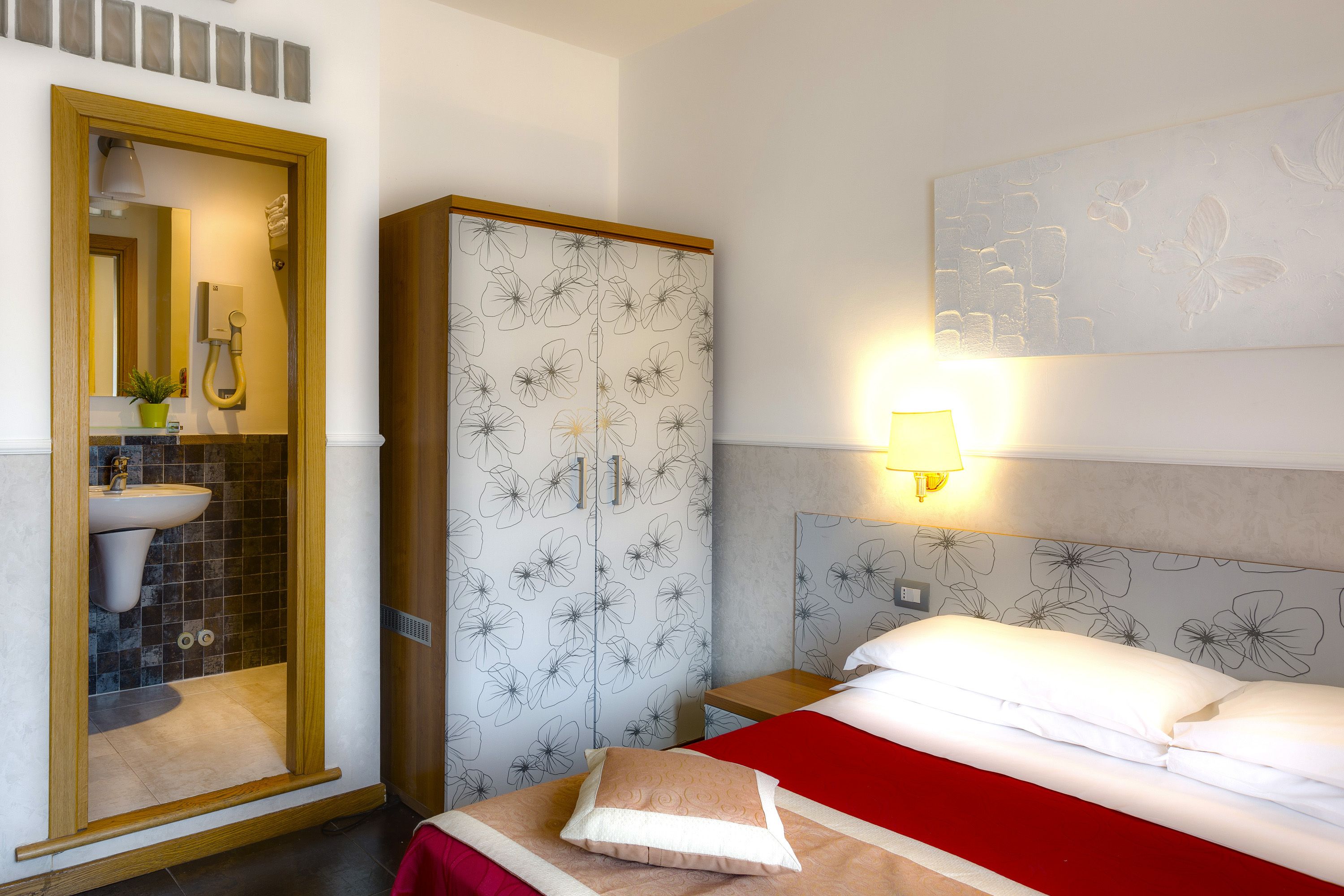 Una habitación de hotel con cama, armario, baño con lavamanos y espejo.