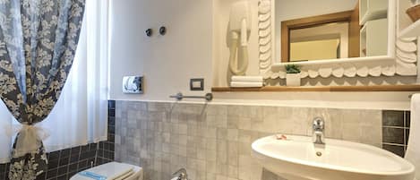 Ein Badezimmer mit Toilette, Bidet und Waschbecken. Ein Handtuchhalter, ein Spiegel und ein Handtuch sind an der Wand angebracht.