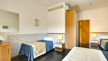 Una camera d'hotel con due letti, un'armadio in legno, un comodino con una lampada e uno specchio a parete.