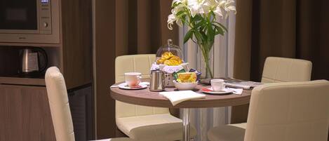 A dining area with a round table, four chairs, a coffee maker, a microwave, and a vase with white flowers.