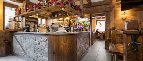 A rustic bar area with a stone counter, wooden beams, and a cozy seating arrangement.