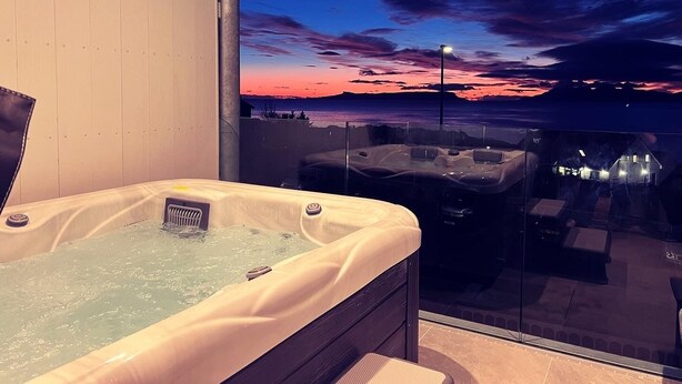 A hot tub with a sunset view through a glass wall. - West Highland Hotel (Mallaig)