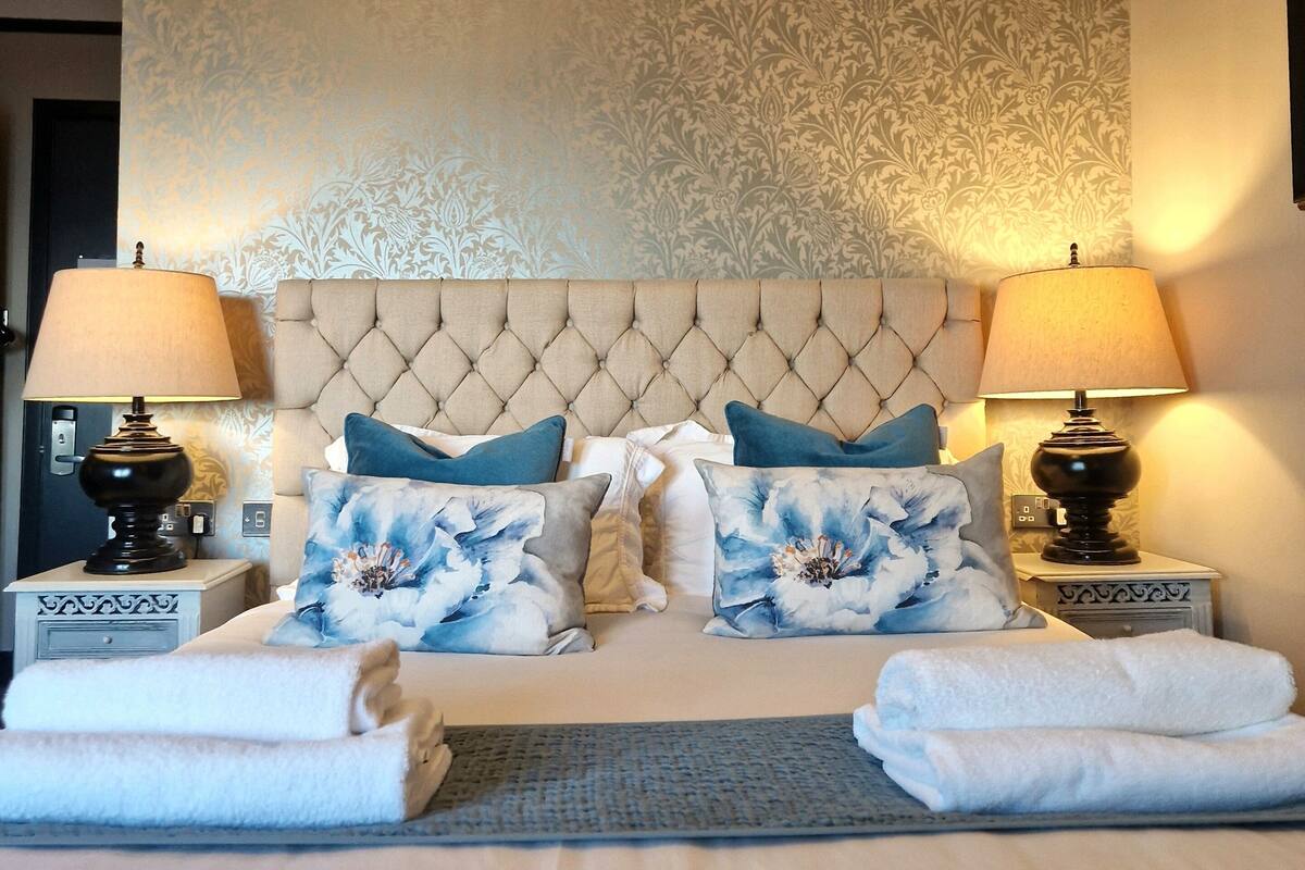 A neatly made bed with a tufted headboard, two bedside tables with lamps, and floral-patterned wall decor.