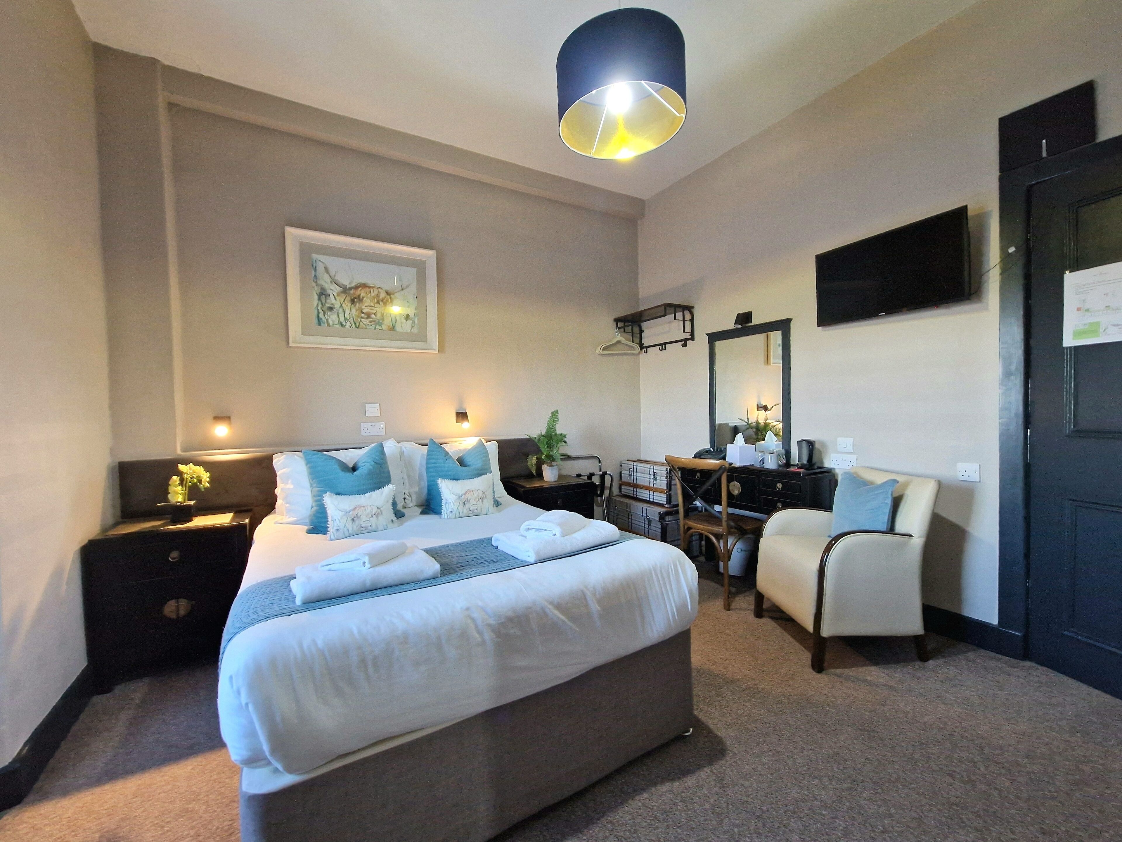 Una habitación de hotel con una cama grande, mesitas de noche, un escritorio con silla, un espejo y un televisor en la pared.