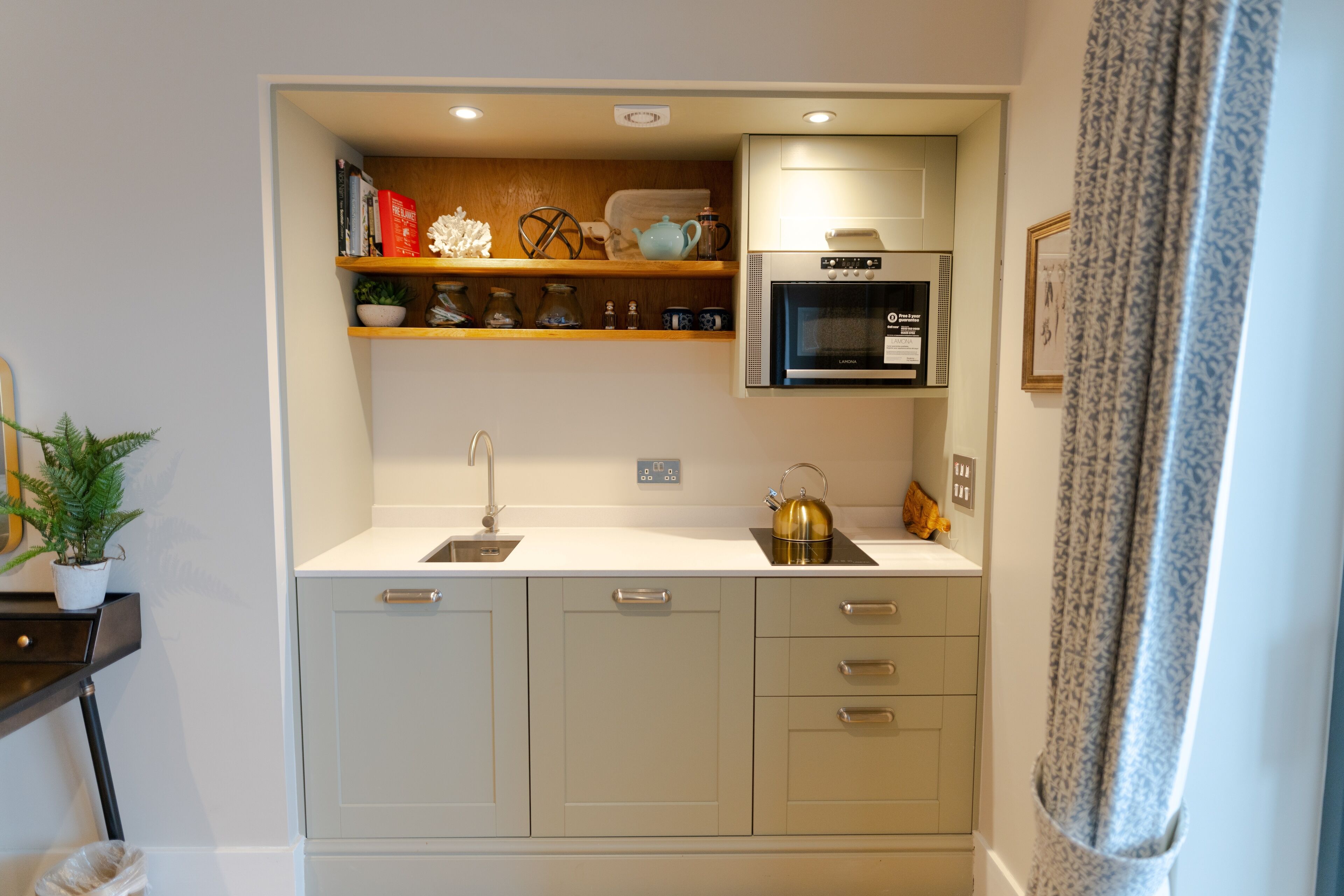 A compact kitchen with a built-in oven, a sink, and a countertop with a kettle and teapot.