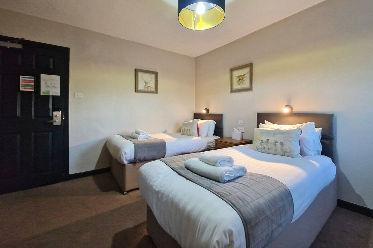 A hotel room with two beds, a dark door, a light fixture, and framed pictures on the walls.