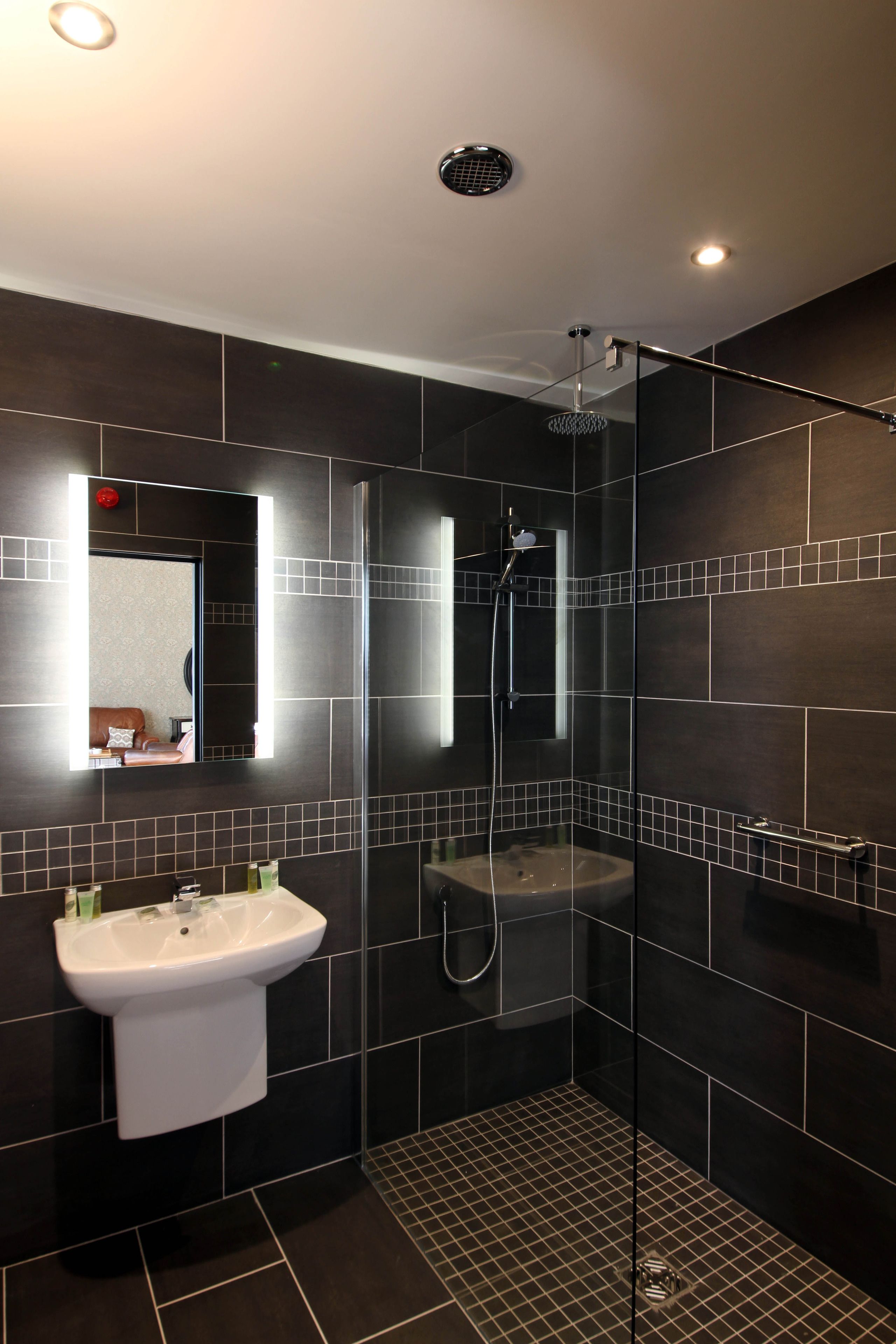 A modern bathroom with dark tiles, a glass-enclosed shower, and a white sink.