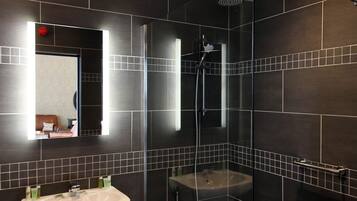 A modern bathroom with dark tiles, a glass-enclosed shower, and a white sink.