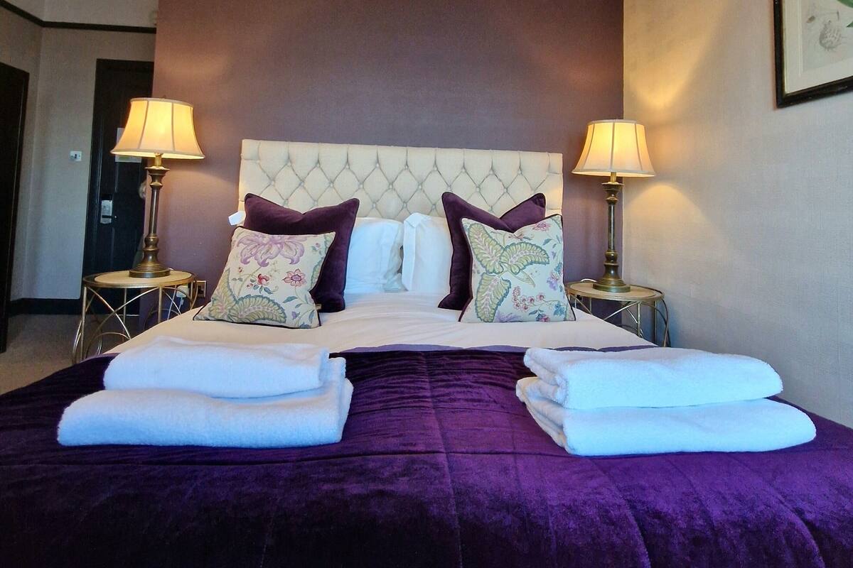 A hotel room with a large bed, two side tables with lamps, and a framed picture on the wall.