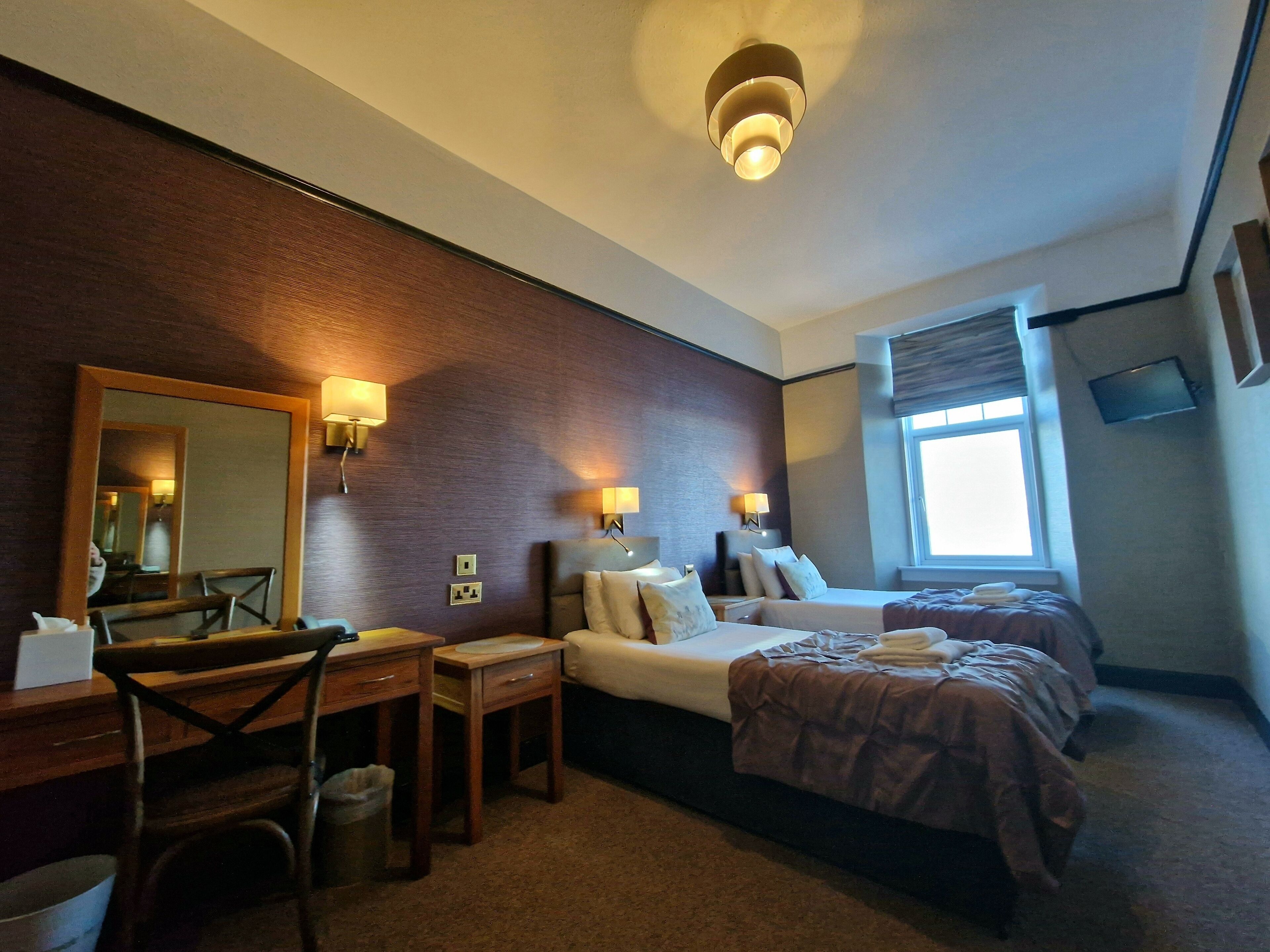A hotel room with two beds, a desk, a chair, a mirror, and a window.