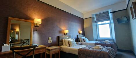A hotel room with two beds, a desk, a chair, a mirror, and a window.