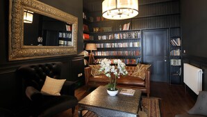 A dark-themed living room with a large mirror, a bookshelf, a leather sofa, and a coffee table with a vase of flowers. - West Highland Hotel (Mallaig)