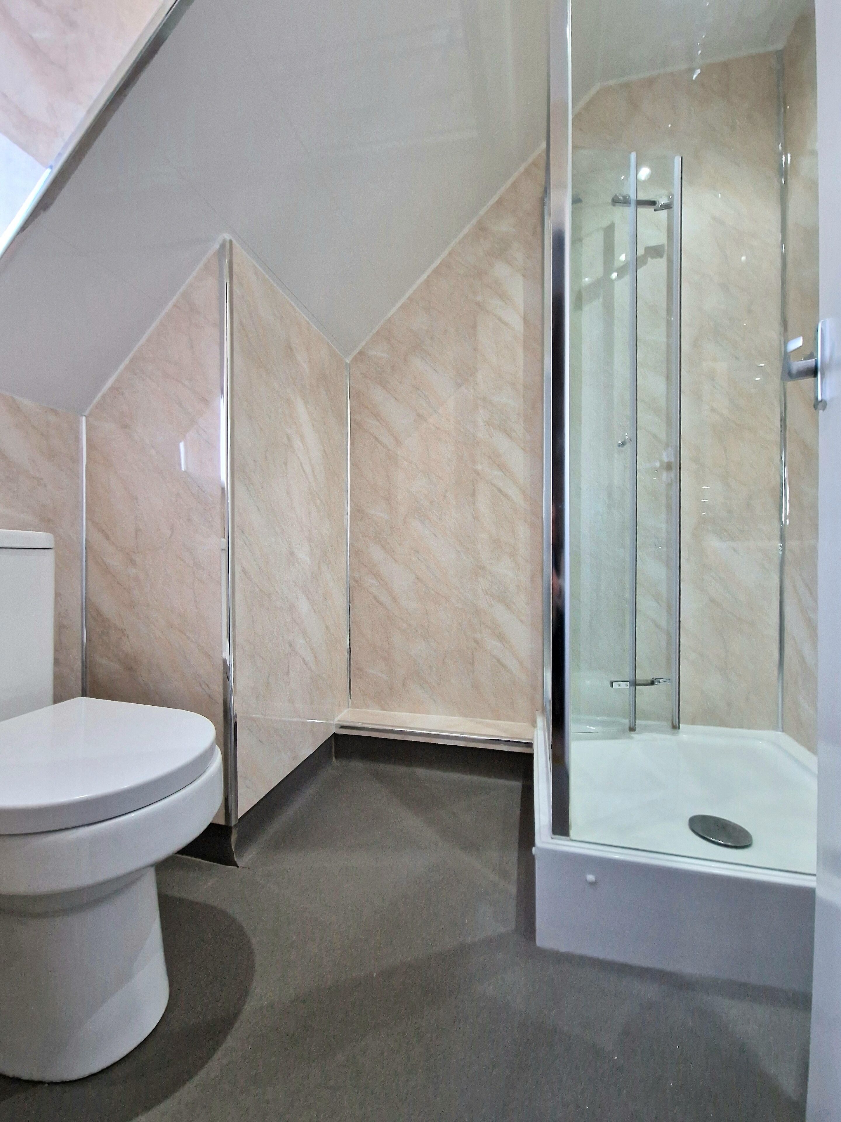 A modern bathroom with a toilet, a shower with glass doors, and marble walls.